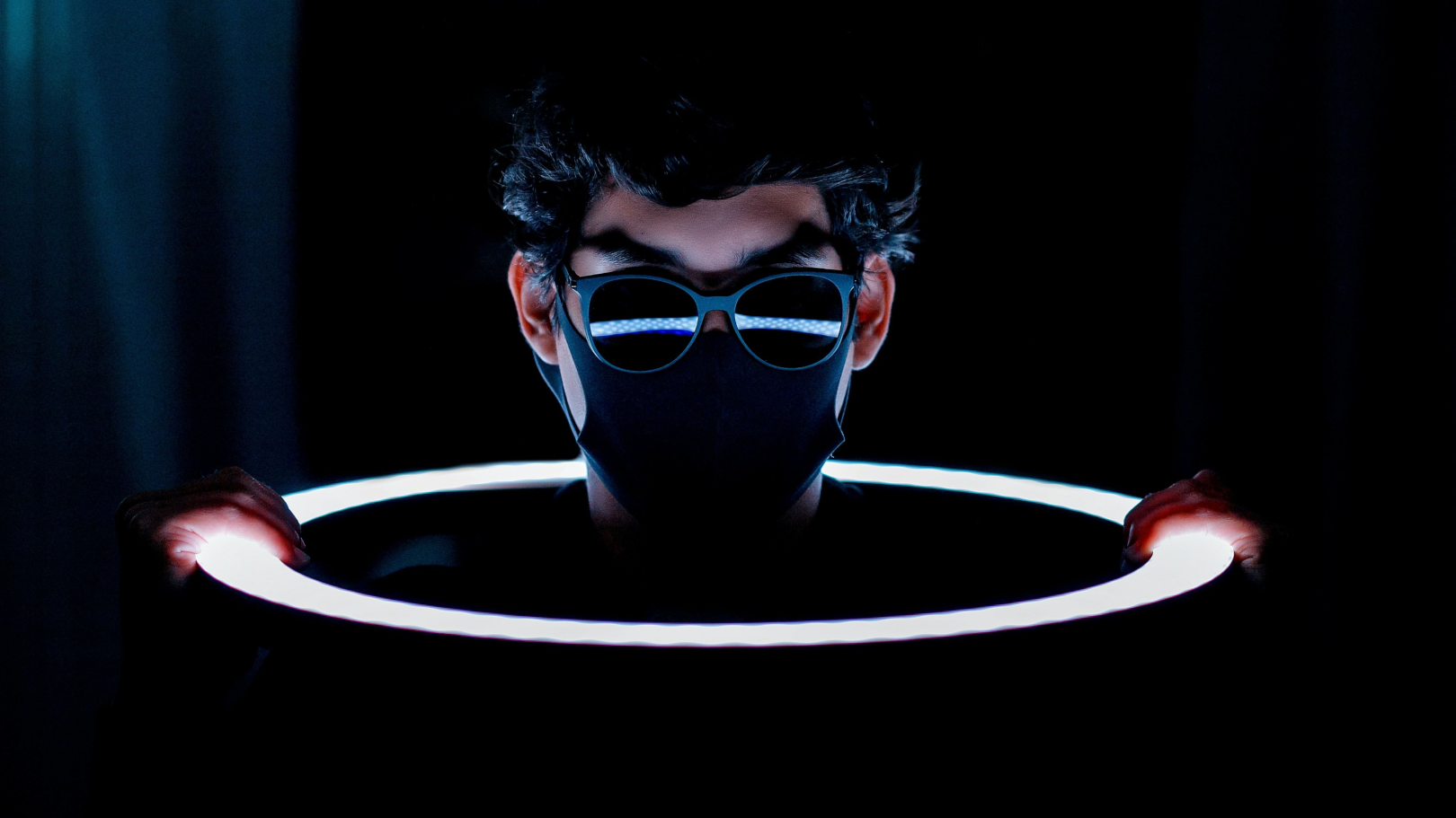 Person mit Maske und Sonnenbrille und einem Leuchtring in den Händen