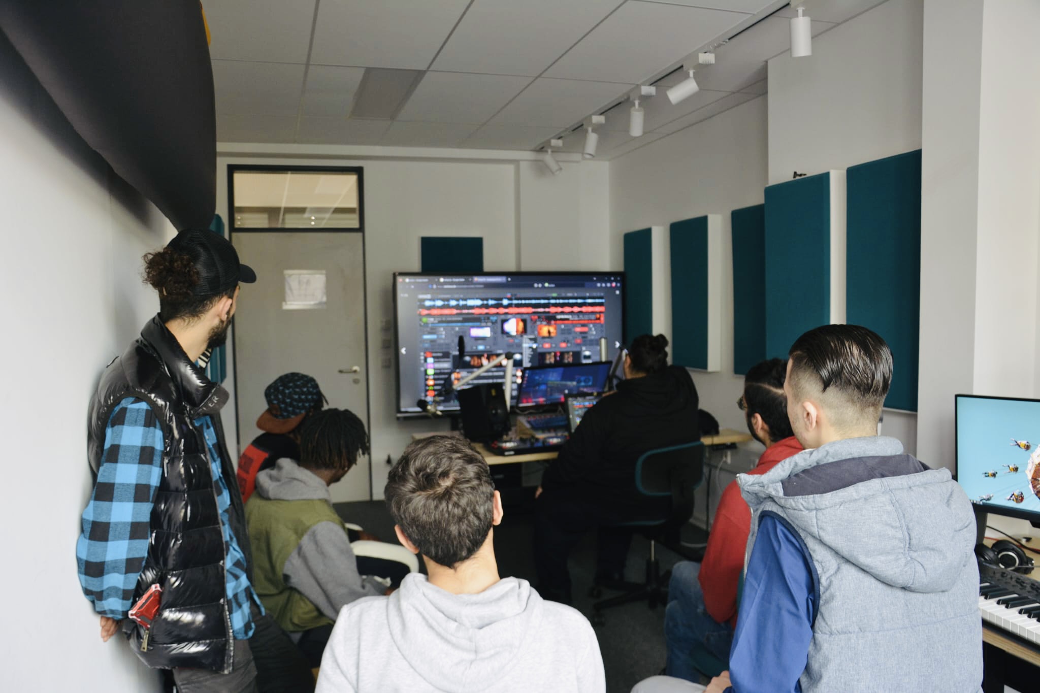 Eine Gruppe junger Männer in einem Radiostudio mit einem großen Bildschirm, auf dem DJ Software zu sehen ist